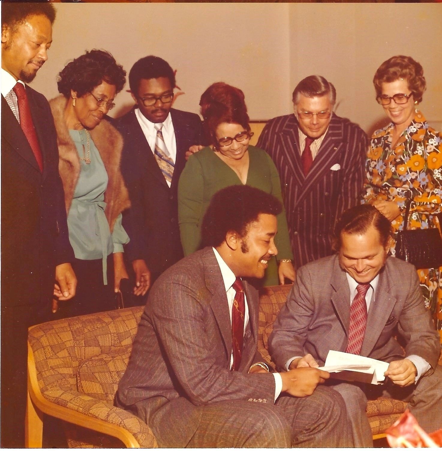 Group of people in formal business attire at a 1970s organizational gathering